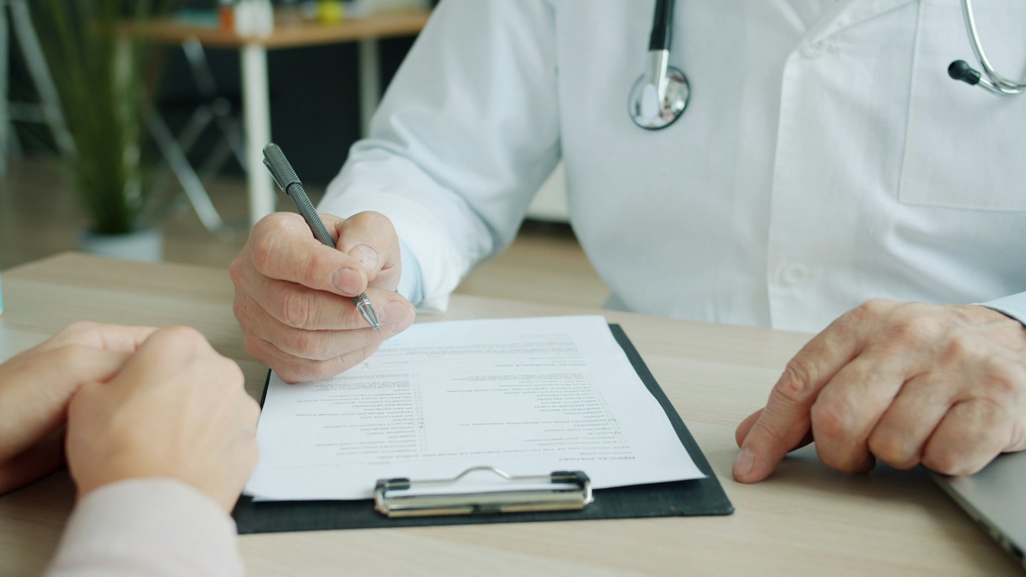 Doctor writes on clipboard during patient consultation.